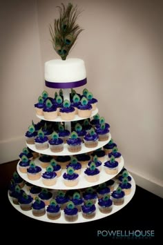 a tiered cake decorated with peacock feathers and cupcakes