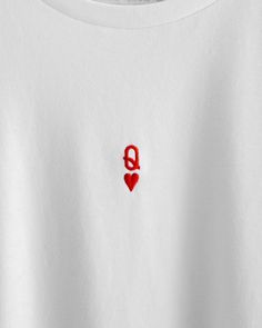 a white t - shirt with a red heart embroidered on the chest and an q in the middle