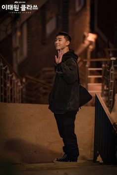 a man standing in front of stairs with his hand on his chin and looking up at the sky