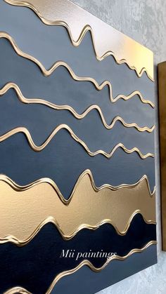 an abstract painting with gold and blue waves painted on it's side by the wall