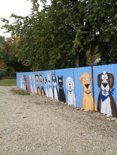 there are many dogs painted on the side of this fence that is next to some trees