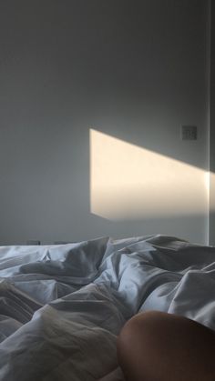 a person laying in bed with the sheets pulled back and sunlight coming through the window