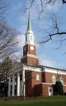 a large brick building with a steeple and clock on it's side, surrounded by trees