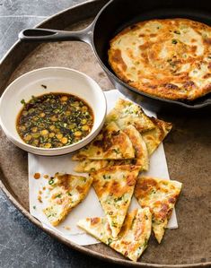 some food is sitting on a plate and next to a skillet with sauce in it