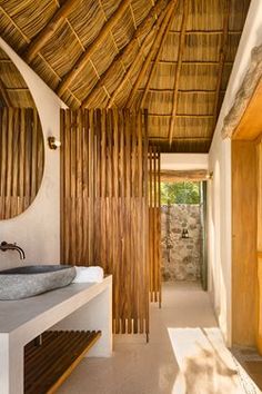 a bathroom with a wooden ceiling and white counter top next to a large round mirror