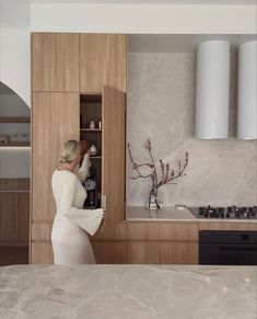 a woman standing in a kitchen next to a stove top oven and counter with a vase on it