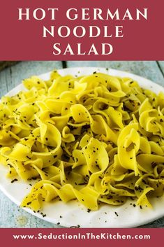 a white plate topped with pasta covered in cheese and seasoning next to a red sign that says hot german noodle salad