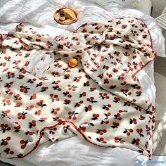 an unmade bed with red and black flowers on it, next to a bottle of orange juice