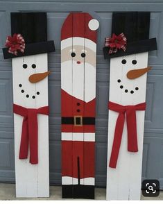 three snowmen made out of wooden planks sitting in front of a garage door