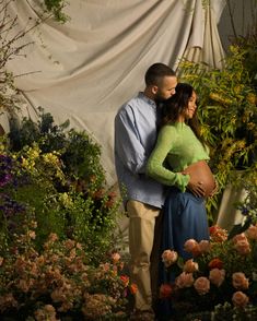 a pregnant woman and man standing in front of flowers with their arms around each other