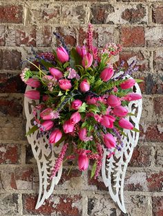 a bouquet of pink flowers sitting on top of a white angel shaped wall mounted plaque