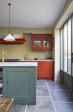 a kitchen with red cabinets and an island in the middle, along with gray tile flooring