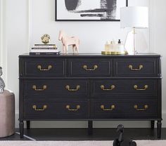 a black dresser with gold handles and knobs in front of a framed art piece