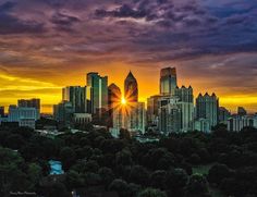 the sun is setting over a city with skyscrapers in the distance and trees below