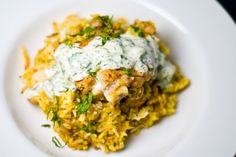 a white plate topped with rice and meat covered in green sauce, garnished with parsley