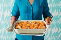 a woman is holding a casserole dish with noodles and meats in it