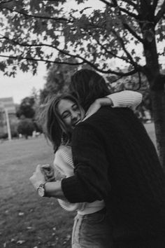 black and white photograph of two people embracing each other in front of a large tree