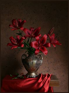 a vase filled with red flowers sitting on top of a table next to a red cloth