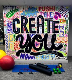 an exercise room with yoga mats, balls, and gym equipment in front of a large sign that reads create you now