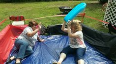 two women sitting on top of a blue tarp