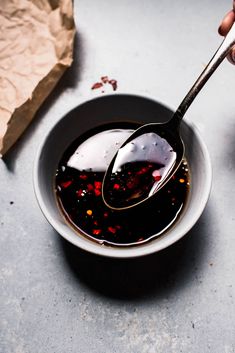 a person holding a spoon in a bowl filled with sauce on top of a table