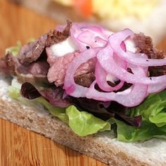 a sandwich with lettuce, onions and meat on it sitting on a cutting board