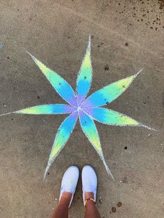 a person standing in front of a blue and green flower on the ground with their feet up