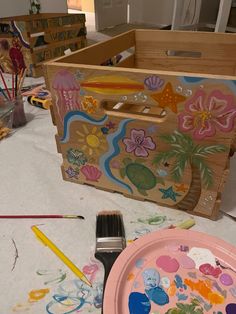 a wooden box sitting on top of a table next to a plate and paintbrush