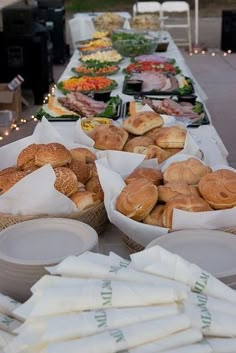 an outdoor buffet table with bread rolls and other food items on the table, ready to be served