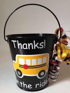 a black bucket with a yellow school bus on it and a ribbon tied around the handle