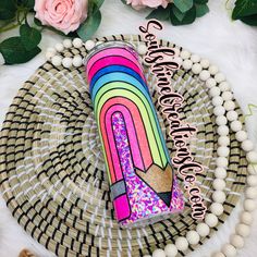 a pink, yellow, and green drink with a rainbow design on it sitting on a wicker plate next to flowers