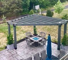 an outdoor patio with table and chairs under a pergolated roof, surrounded by lush green trees