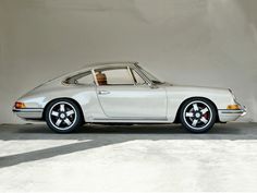 an old white porsche parked in front of a wall with shadows on the floor and walls behind it