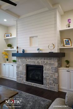 a living room with a stone fireplace and built - in shelving