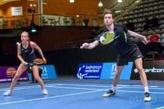 two people playing tennis on a blue court with spectators in the bleachers behind them