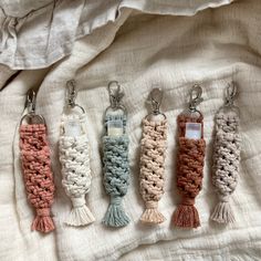 four crocheted keychains with tassels are lined up on a bed