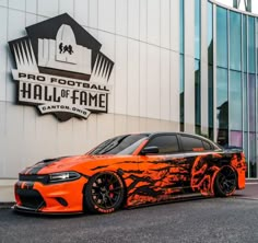 an orange sports car parked in front of a football hall of fame building with flames painted on it