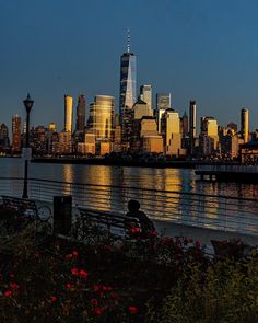 the city skyline is lit up at night as people sit on benches by the water