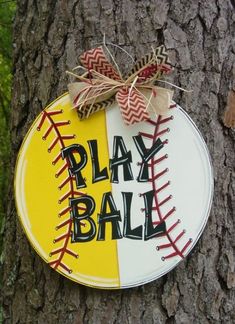 a sign that says play ball on the side of a tree with a bow around it