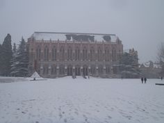 two people walking in front of a large building covered in snow