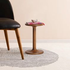 a small table with a cup on it next to a black chair and white rug