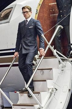 a man in a suit walking up the stairs to an airplane with another man standing next to him