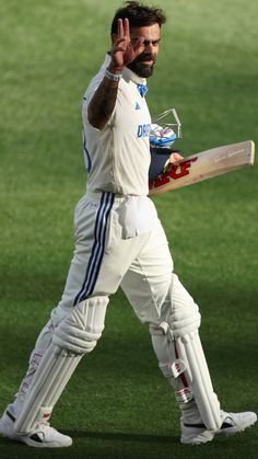 a man holding a cricket bat on top of a grass covered field with his hand in the air