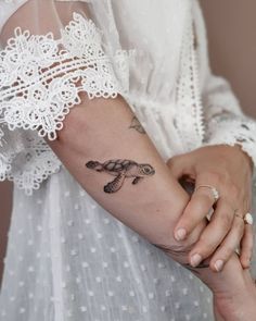 a woman with a tattoo on her arm holding onto another person's hand and wearing a white dress