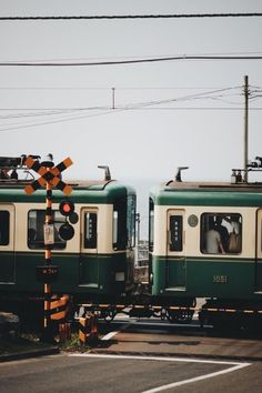 two green and white trains sitting next to each other on train tracks with power lines above them