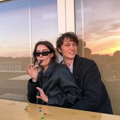 a man and woman sitting at a table in front of a window with the sun setting behind them