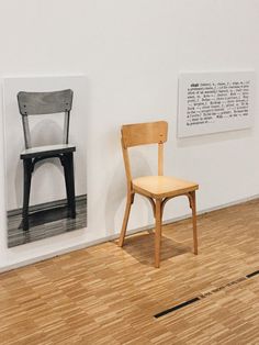 a wooden chair sitting next to a black and white photo on the wall in an art gallery