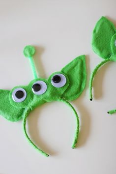 two green hats with googly eyes are on a white surface next to each other