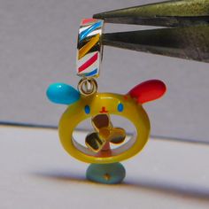 a pair of scissors cutting through a small yellow animal keychain with colorful beads on it