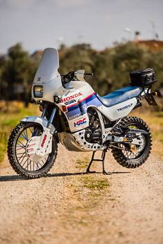 a white and blue motorcycle parked on top of a dirt road next to a field